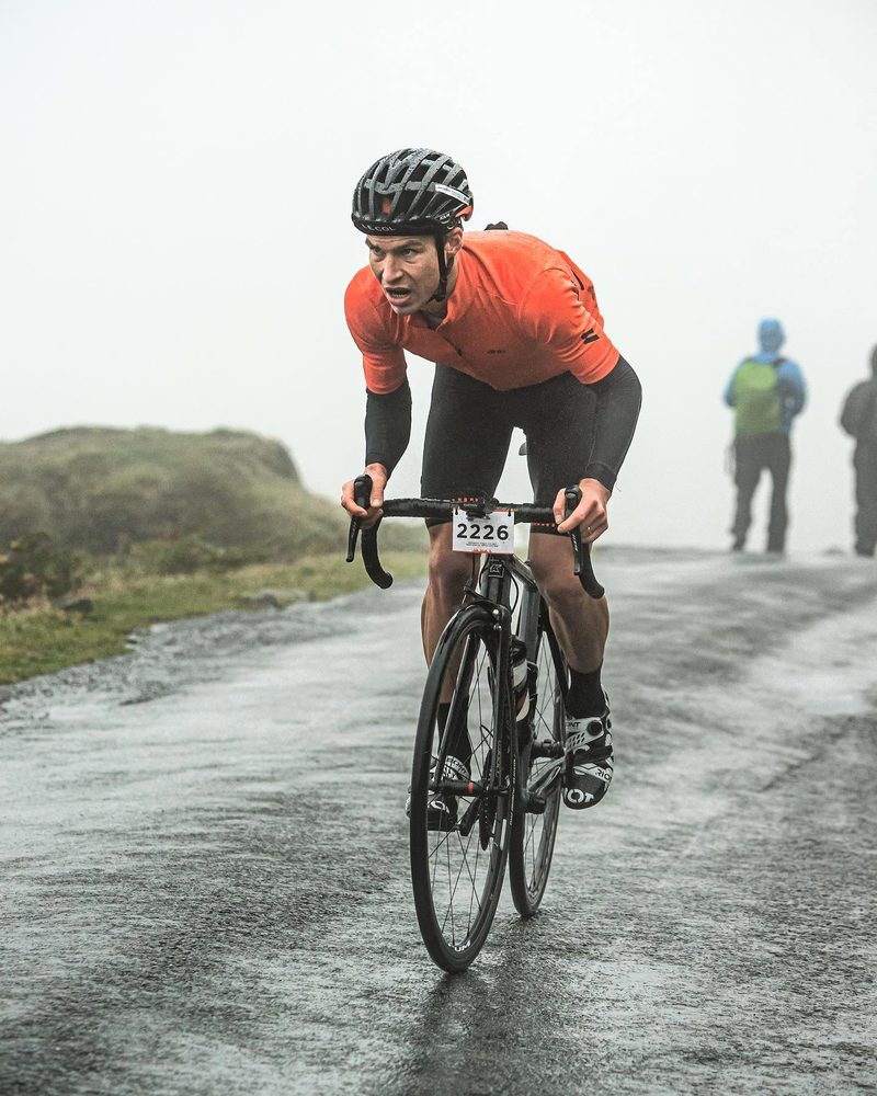 Brennan Townshend climbing out of the saddle on his road bike in the rain during a race