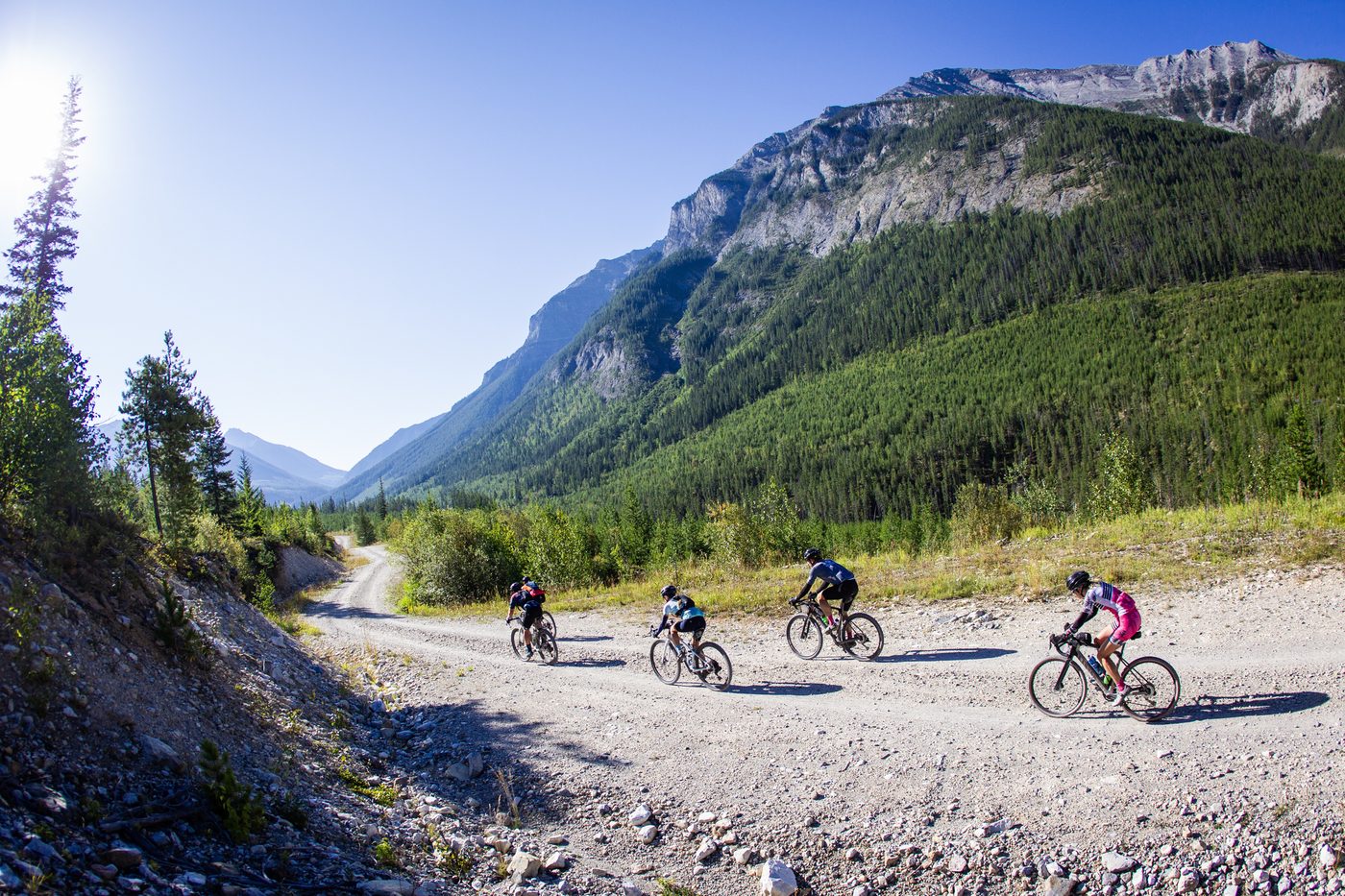 Four riders strung out along a gravel road beneath forested mountains at the TransRockies Gravel Royale in British Columbia