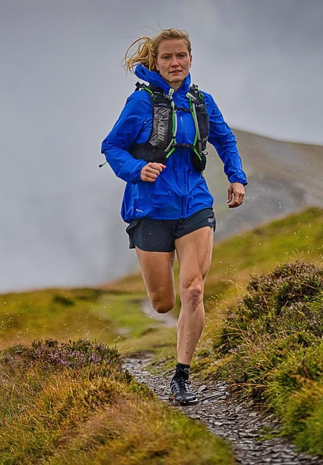 Kat Townshend running along a fell path in the Lake District in a blue jacket