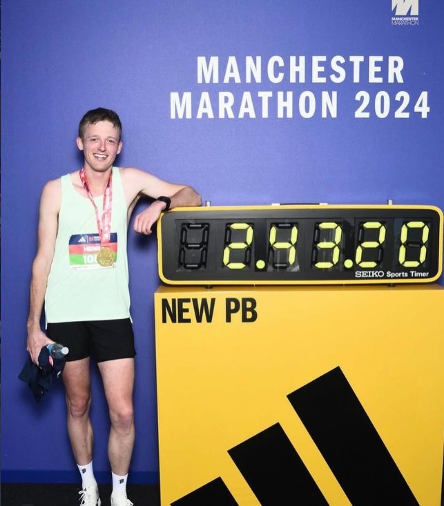 Henry beside the finish clock showing his 2:43:20 personal best at the Manchester Marathon 2024